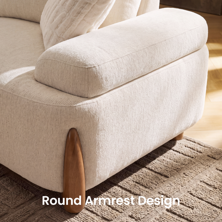 Close-up of a cream upholstered sofa with a rounded padded armrest, textured upholstery, a brown tapered leg, and a cream cushion on a patterned rug.