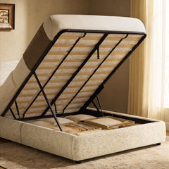 Cream upholstered bed with its mattress and slatted base lifted to reveal storage compartments containing pillows and folded blankets.