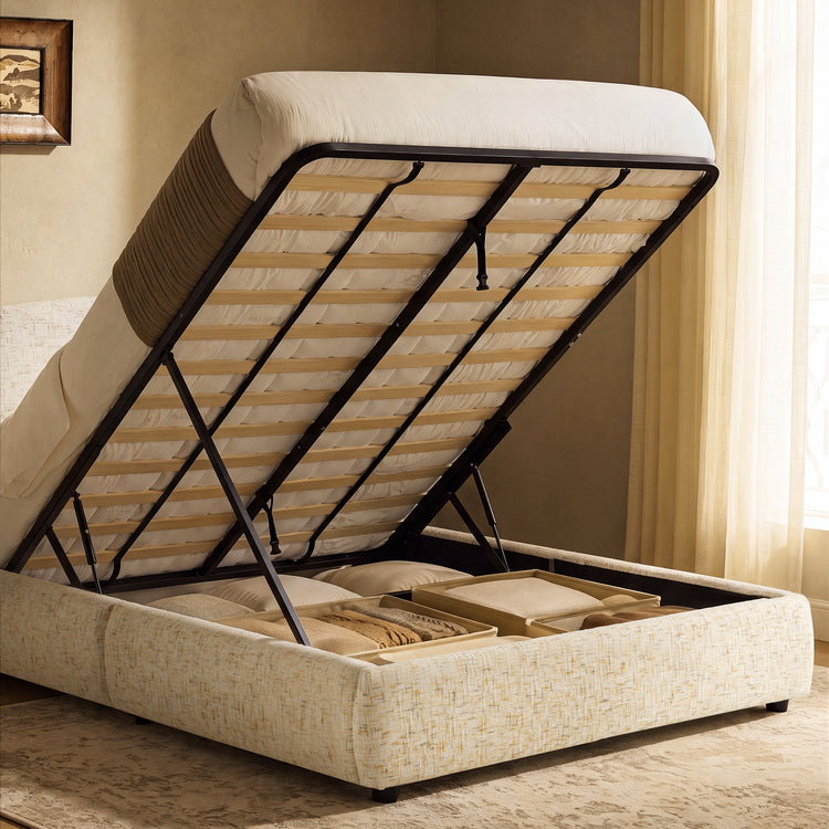 Cream upholstered bed with its mattress and slatted base lifted to reveal storage compartments containing pillows and folded blankets.