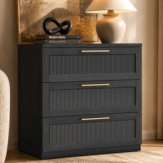 Black three-drawer chest with fluted inset panels and gold-tone pulls beneath a lamp and framed artwork