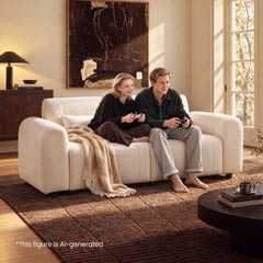 Two people holding game controllers sit on a cream sofa with a beige throw in a sunlit living room with abstract wall art and a brown patterned rug.