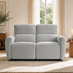 Front view of a light gray loveseat with two tall padded backs and rounded arms beside a living room window