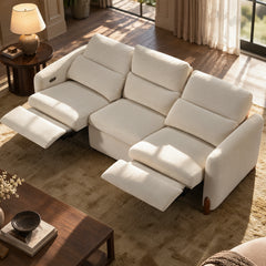 Cream three-seat sofa with two footrests extended in a sunlit living room.