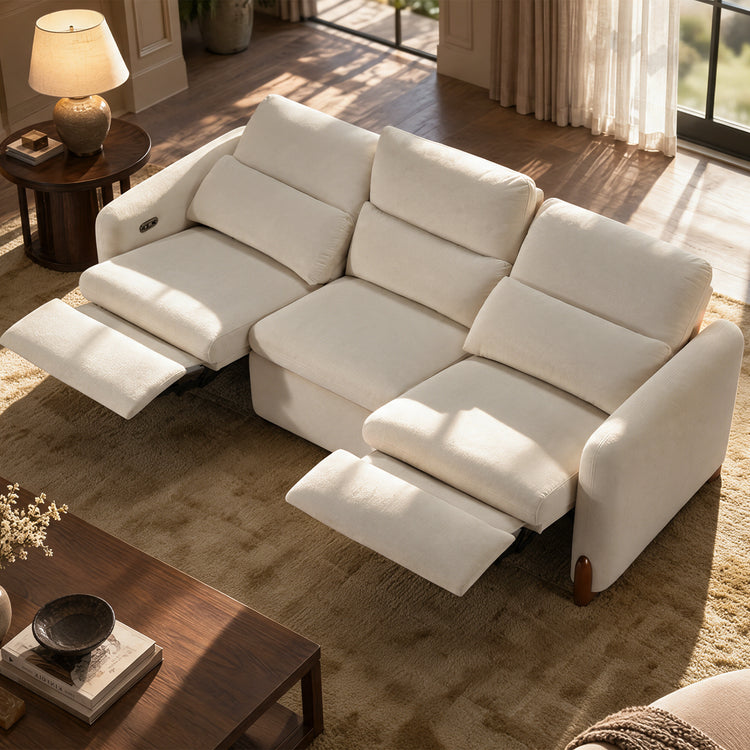 Cream three-seat sofa with two footrests extended in a sunlit living room.